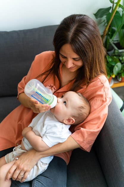 Photo closeup of a mother holding her baby in her arms and feeding her bottle while looking at each other indoors