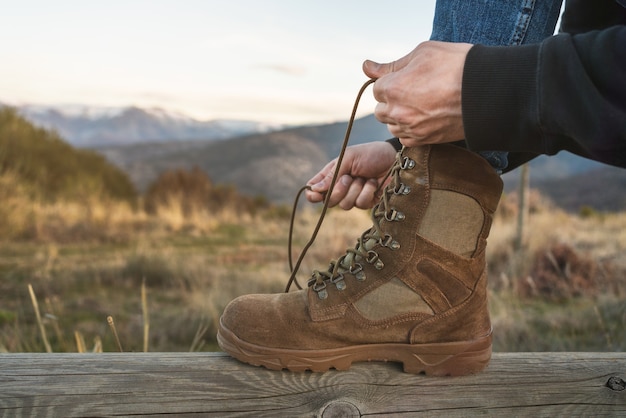 Photo closeup of a mountaineer tying brown boot laces with snowy mountains in the wall