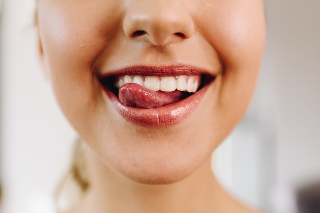 Primo piano della bocca di giovane bella donna caucasica che sorride e che ha la sua lingua fuori, sfacciato, felice. denti bianchi perfetti. ottime condizioni della pelle. la ragazza indossa rossetto rosso.