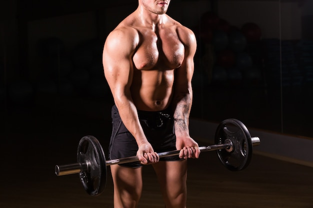 Closeup of a muscular young man lifting weights on dark wall