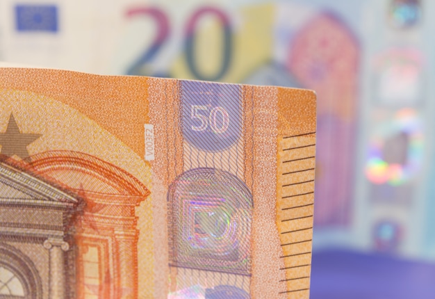 Closeup of new banknote of fifty euros with another twenty bill, out of focus in the background.