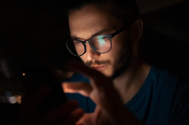 Closeup night portrait of thoughtful young man touching screen of smartphone