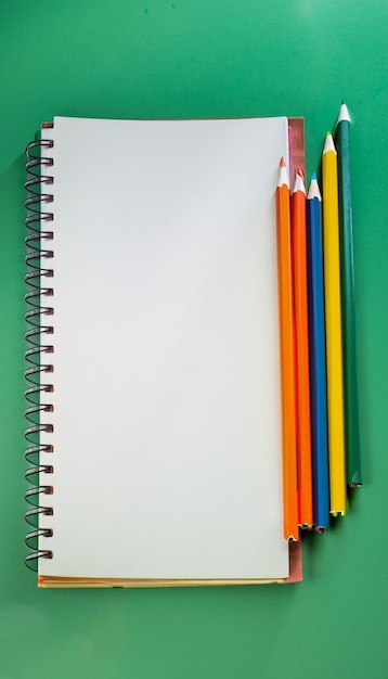 Closeup Notebook and colored pencils on a green board background