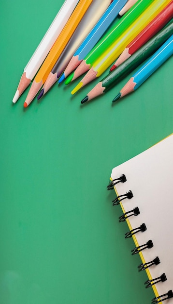 Closeup Notebook and colored pencils on a green board background