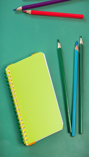 Клоуз-ап блокнот и цветные карандаши на зеленом фоне доски