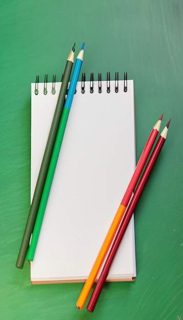 Closeup Notebook and colored pencils on a green board background