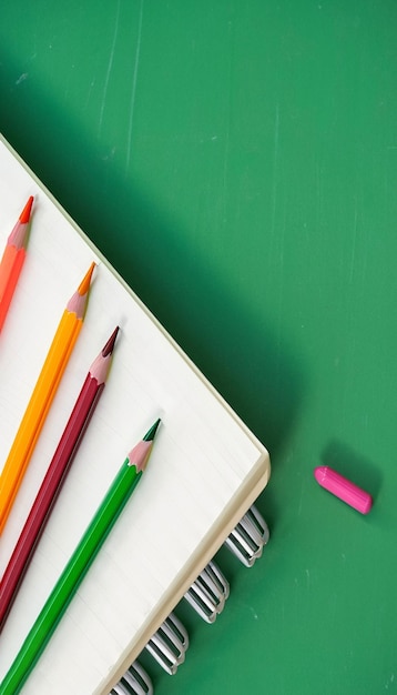 Closeup Notebook and colored pencils on a green board background