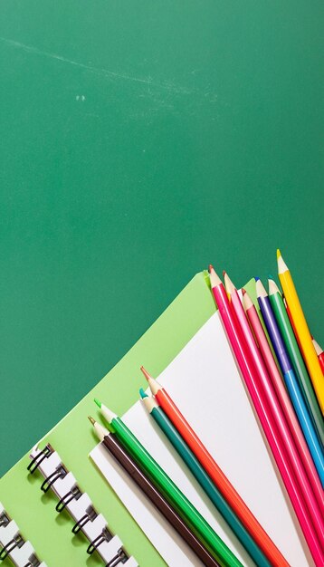 Closeup Notebook and colored pencils on a green board background