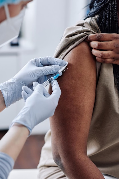 Closeup of nurse in protective gloves using syringe to vaccinate african girl at hospital