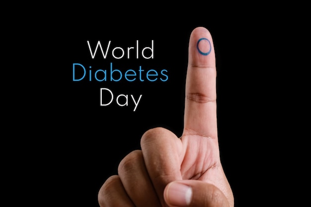 사진 그의 집게 손가락에 파란색 원, 당뇨병의 상징, 그리고 검은 배경 위에 텍스트 세계 당뇨병의 날을 가진 젊은 아시아 남자 앞 손가락의 근접 촬영