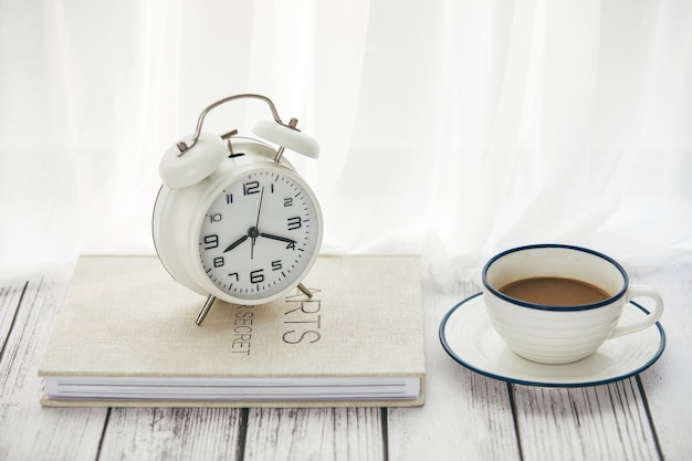 写真 テーブルの上のコーヒーとメモ帳の目覚まし時計のクローズアップ