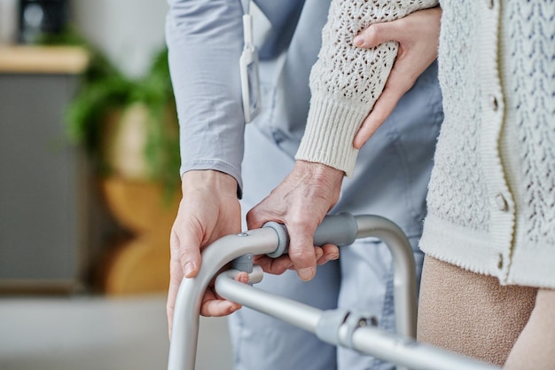 Фото Крупный план сиделки, помогающей пожилой женщине ходить с помощью ходунков
