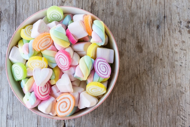 木製のテーブル背景やテクスチャの上にボウルにお菓子とカラフルなミニマシュマロのクローズアップ。