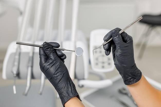 Фото Крупный план рук женщин-врачей в черных перчатках, держащих зонд стоматологических инструментов и концепцию зеркала