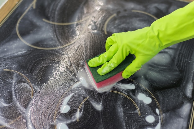 スポンジと洗剤で現代の調理ガラスセラミック電気表面を掃除する手の女性のクローズアップ