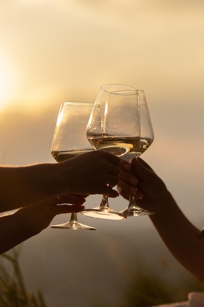 写真 日没時に白ワインの入ったグラスを持つ手のクローズアップ
