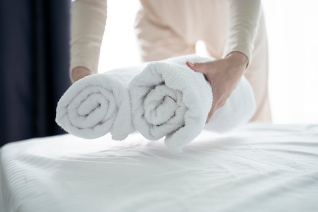 Фото Близкий снимок рук, кладущих стоп свежих белых полотенец для ванны на простыню.