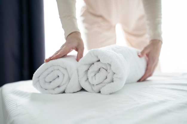 Фото Близкий снимок рук, кладущих стоп свежих белых полотенец для ванны на простыню.