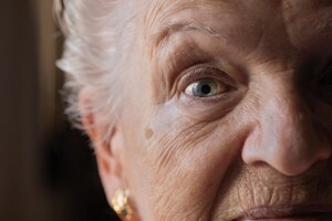 closeup of the gaze of an elderly grayhaired woman with blue eyes and a face wrinkled by old age.