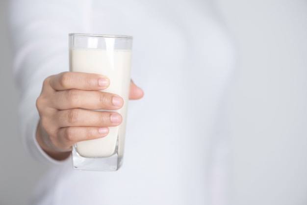写真 白い背景の上に新鮮な牛乳のガラスを持つ女性の手のクローズアップ