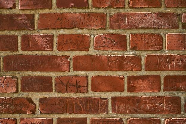 Closeup of an old red brick wall with carvings and copyspace Zoom in on different size shape and patterns of bricks Details of built structure with rough surface sketched or scratched markings