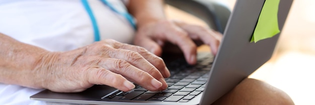 Primo piano delle mani della donna anziana che digitano sul computer portatile moderno femminile anziano che digita sul lavoro a distanza del computer portatile