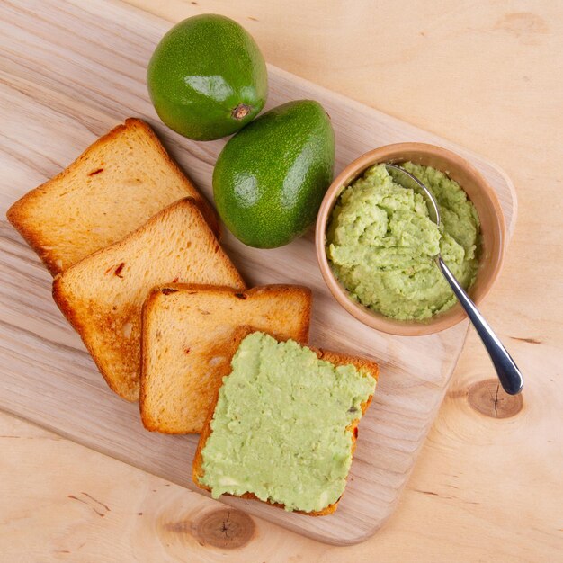 Foto closeup di pane tostato sandwich aperto con spread di avocado e un paio di frutti di avocado su legno piatto