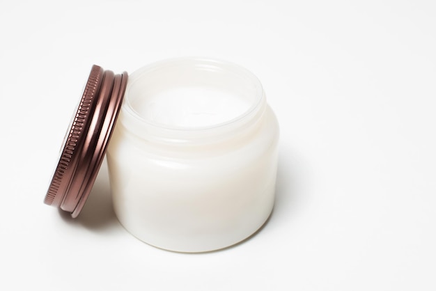 Closeup of opened jar of cosmetic cream near cap on white background