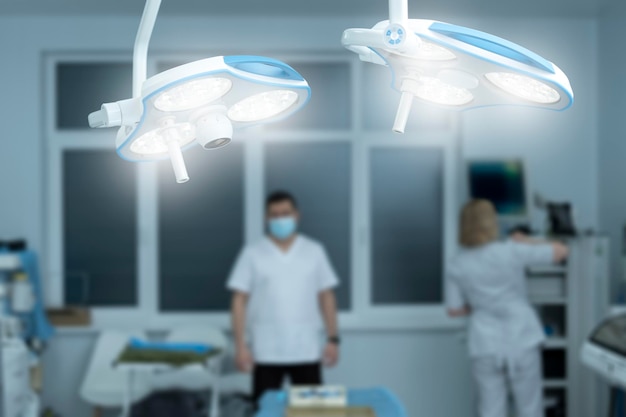 Primo piano lampada operativa accesa in sala operatoria personale medico medico e infermiere su sfondo sfocato moderna sala operatoria preparazione per la chirurgia