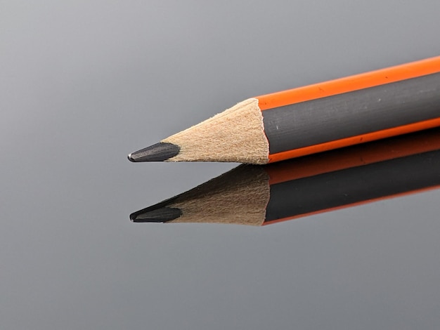 Photo closeup of orange and gray pencil with reflection on black acrylic board
