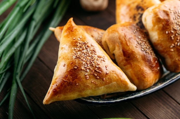 Closeup on oriental dish baked pie with meat triangle samsa on the black stone plate