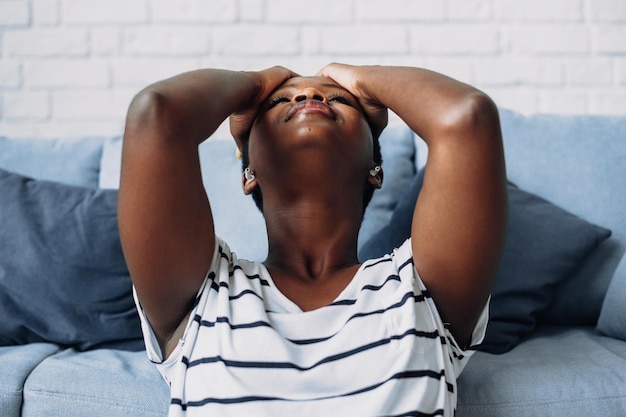 Closeup ortrait of an exhausted african american woman grabbing\
her head feeling stress suffering fr...