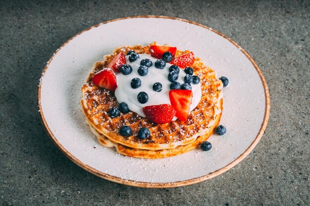 Closeup of pancakes with cream and berries served on a white plate