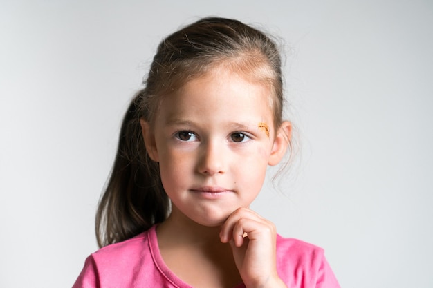 Closeup pensive lovely blond little child girl with injury\
scratch with iodine on face on white background child abuse