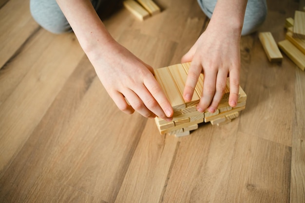 クローズアップの人が床にデザイナーの木製ブロックを積み重ねる子供の手ボードゲームe