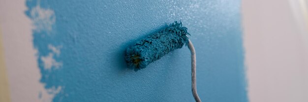 Closeup of person with bright blue paint blue paint on white wall home renovation work and