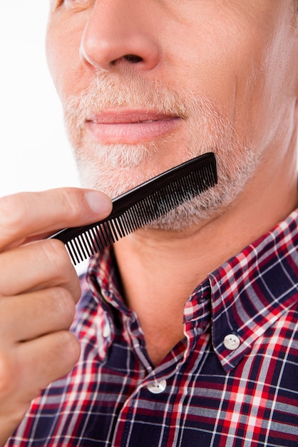 Closeup photo of an aged man combing his beard