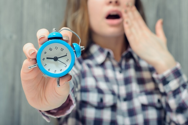 Photo closeup photo of alarm clock in hand and yawning woman on wall