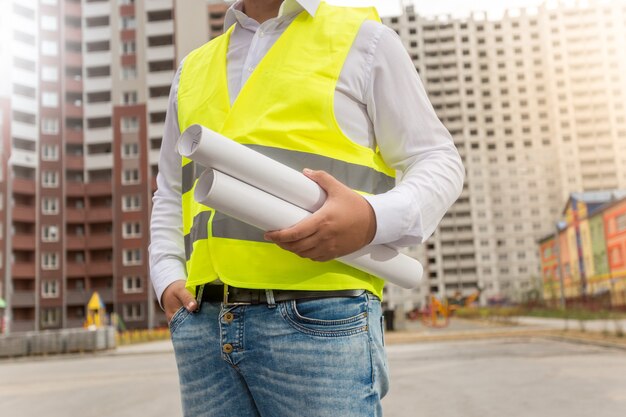 Primo piano dell'architetto in giubbotto di sicurezza in posa con progetti di nuovi edifici