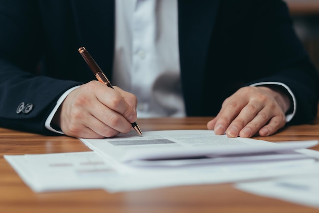 Closeup photo of Asian businessman's hands signing bank documents man working in modern office sitting at table banker's paperwork