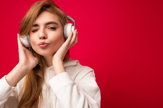 Foto del primo piano di una giovane donna bionda positiva carina attraente che indossa una felpa con cappuccio bianca isolata sopra