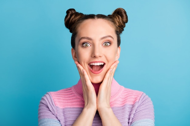 Closeup photo of attractive excited lady two funny buns open mouth good mood charming nice youngster hold arms on cheeks wear casual warm sweater isolated blue color background