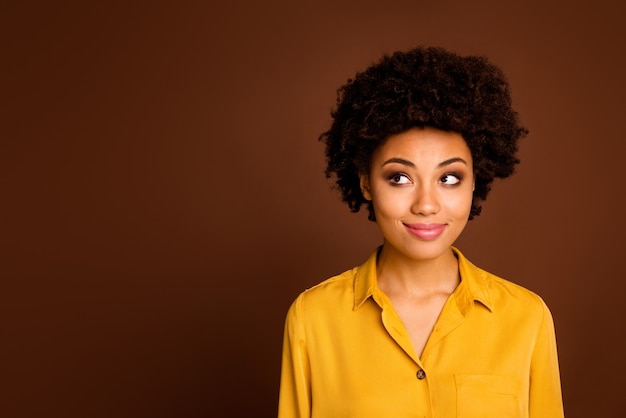 Closeup photo of beautiful pretty dark skin wavy lady positive good mood look side empty space interested have creative idea wear yellow shirt isolated brown color