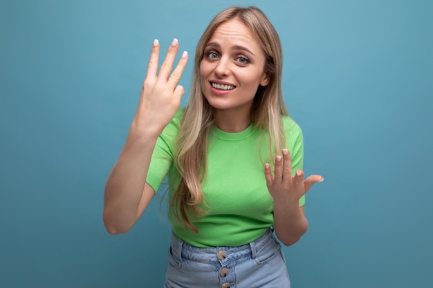 Closeup photo of a blonde young woman in a casual outfit showing three fingers on a blue background