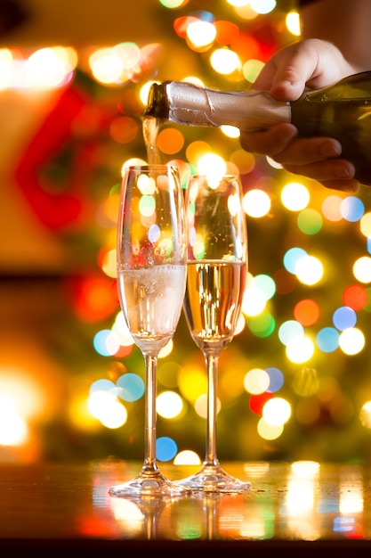 Closeup photo of champagne being poured in glasses against Christmas lights