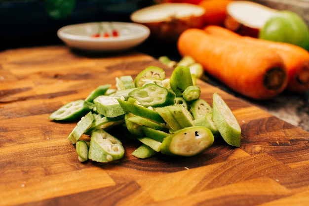 Closeup photo of chopped okra on wooden cutting board with vegetables in the background