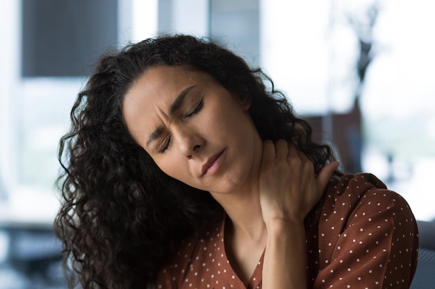 Closeup photo of curlyhaired woman at home near the window with severe neck pain mulatto business