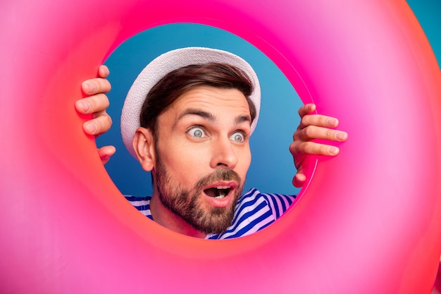 Closeup photo of excited interested funny guy open mouth tourist look inside pink rubber float lifebuoy see sale prices wear striped sailor shirt cap isolated blue color