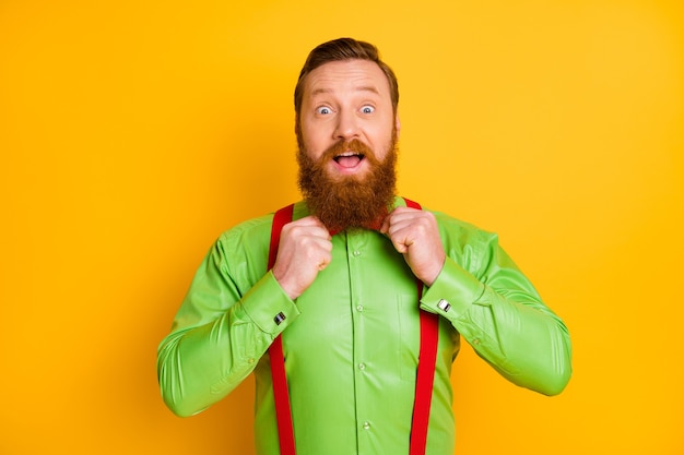 Closeup photo of excited red head guy elegant stylish clothes fixing necktie look mirror preparing party wear bright green shirt red suspenders bow tie isolated vibrant color