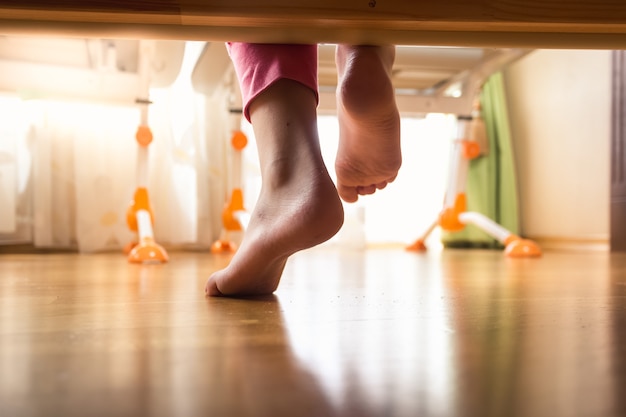 Closeup photo of female feet under the bed on wooden floor